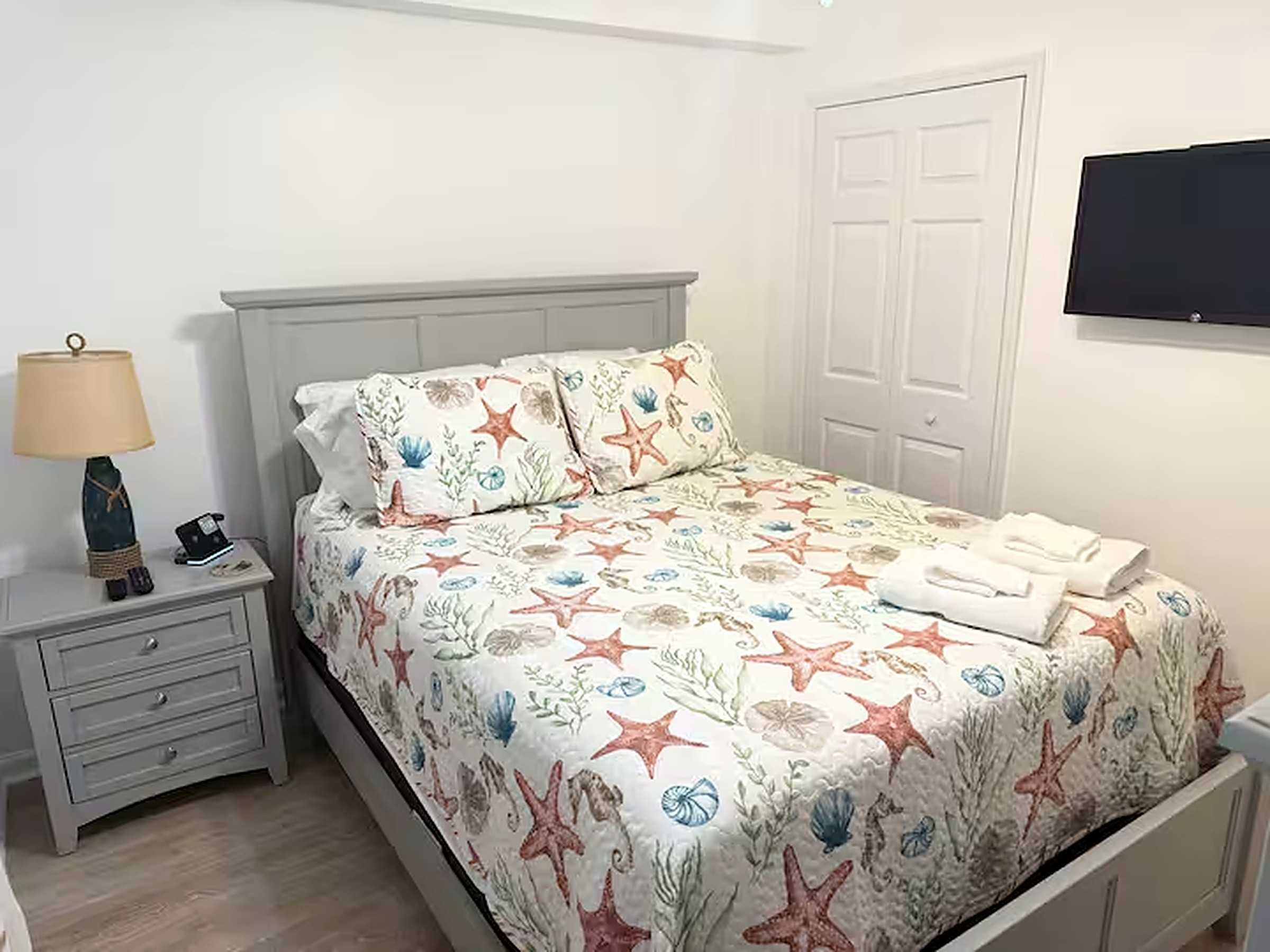 Guest bedroom with queen bed, coastal bedding, grey furniture and a wall-mounted TV